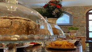 Een eettafel met een taart op een presentatieplateau, een glazen schaal en een bord met eten. Achtergrond met bloemen en een raam.