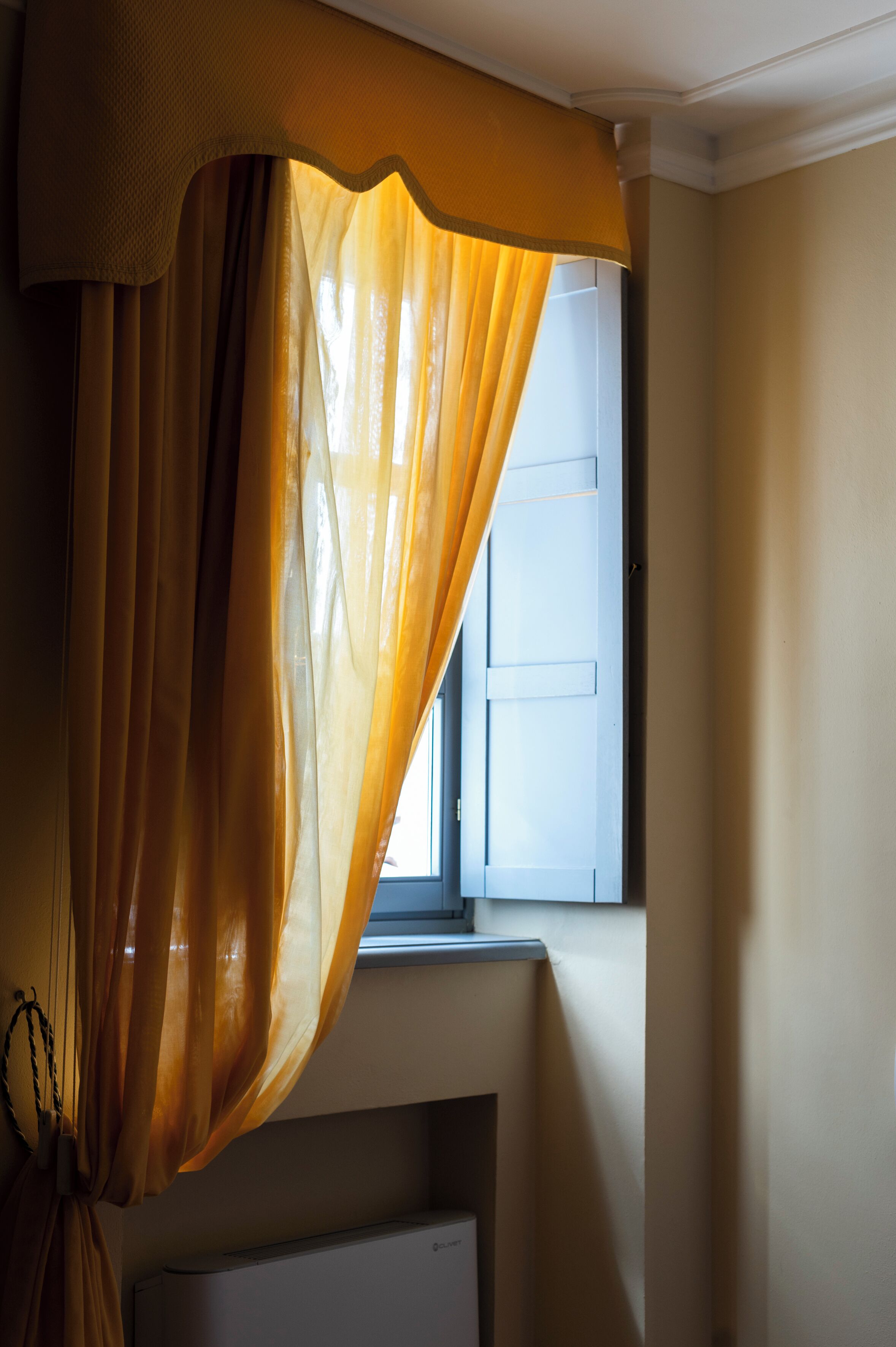 Une pièce avec une fenêtre, un radiateur et un rideau.