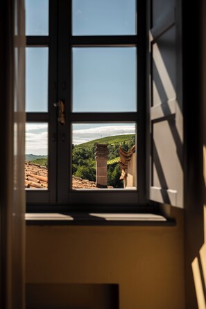 A window with a view of a green landscape and a stone structure. - Albergo Castiglione Langhe (Castiglione Tinella)