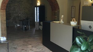 Een receptiegedeelte met een bakstenen boog, een receptiebalie, een zithoek met stoelen en een kamerplant.