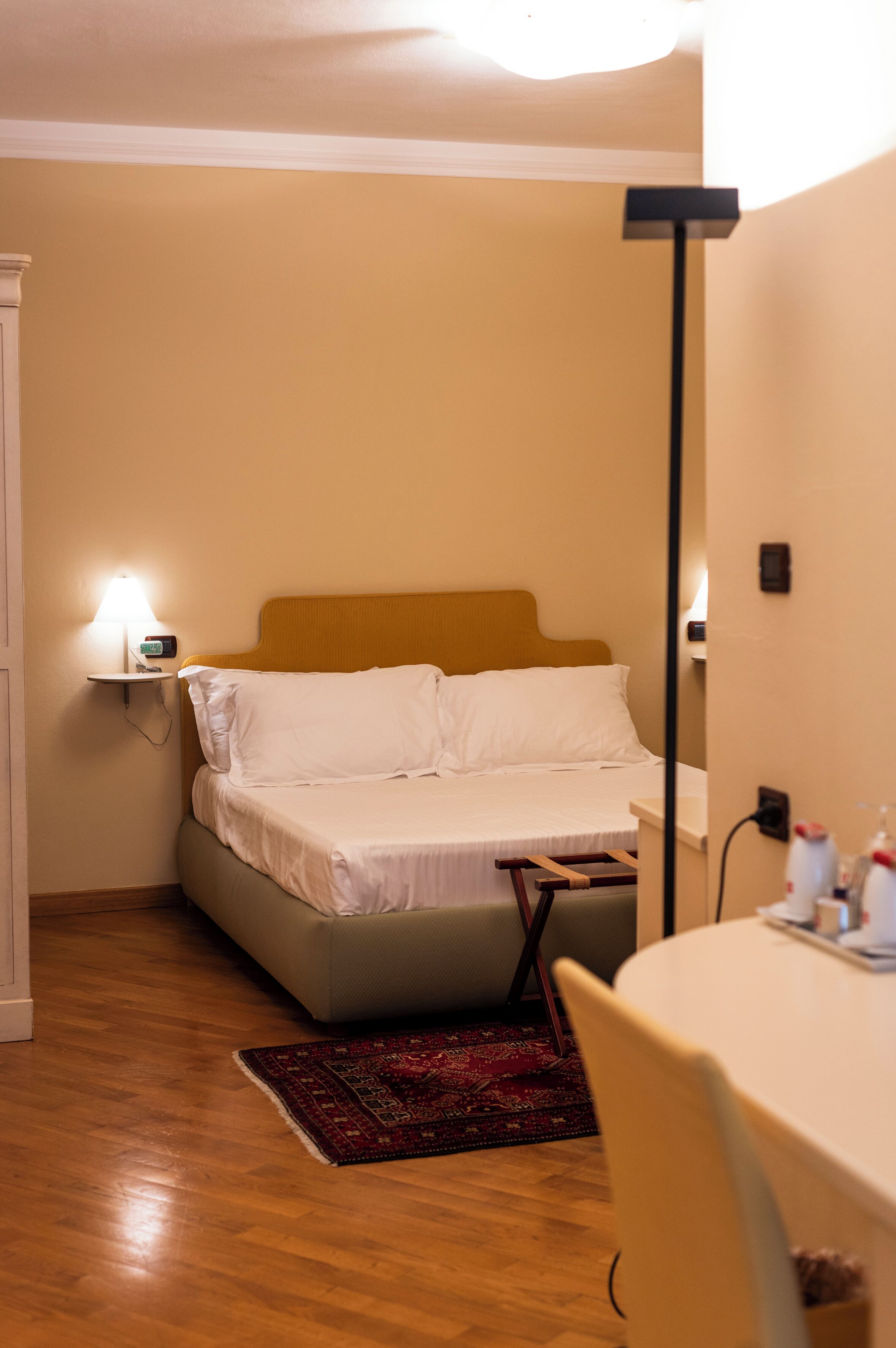 A bedroom with a bed, bedside lamp, and a small table with a chair.