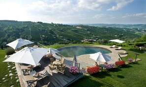 A pool area with a wooden deck, outdoor furniture, and umbrellas. - Albergo Castiglione Langhe (Castiglione Tinella)