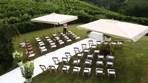 Een evenement buiten met rijen stoelen en tafels, grote parasols, en een persoon die staat.