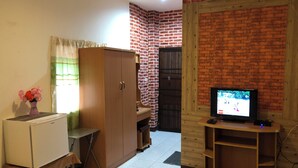 A compact living space with a TV, a small table, a wardrobe, and a brick wall. - Sandee Place Chomthong (Chom Thong)