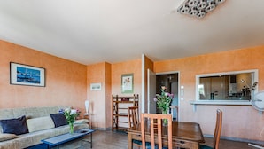 A living room with a sofa, coffee table, dining table, and chairs. There is a painting on the wall and a window with a view. - Convenient Arcachon T2 Apt - Balcony, Elevator, Secure Garage Near Shops & Train Station (Arcachon)