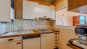 A modern kitchen with a dishwasher, stove, and window overlooking a cityscape. - Convenient Arcachon T2 Apt - Balcony, Elevator, Secure Garage Near Shops & Train Station (Arcachon)