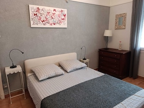 A bedroom with a bed, two bedside tables, a dresser, a lamp, a decorative mirror, and a butterfly artwork on the wall. - Homerez - Apartment in Arles (Arles)