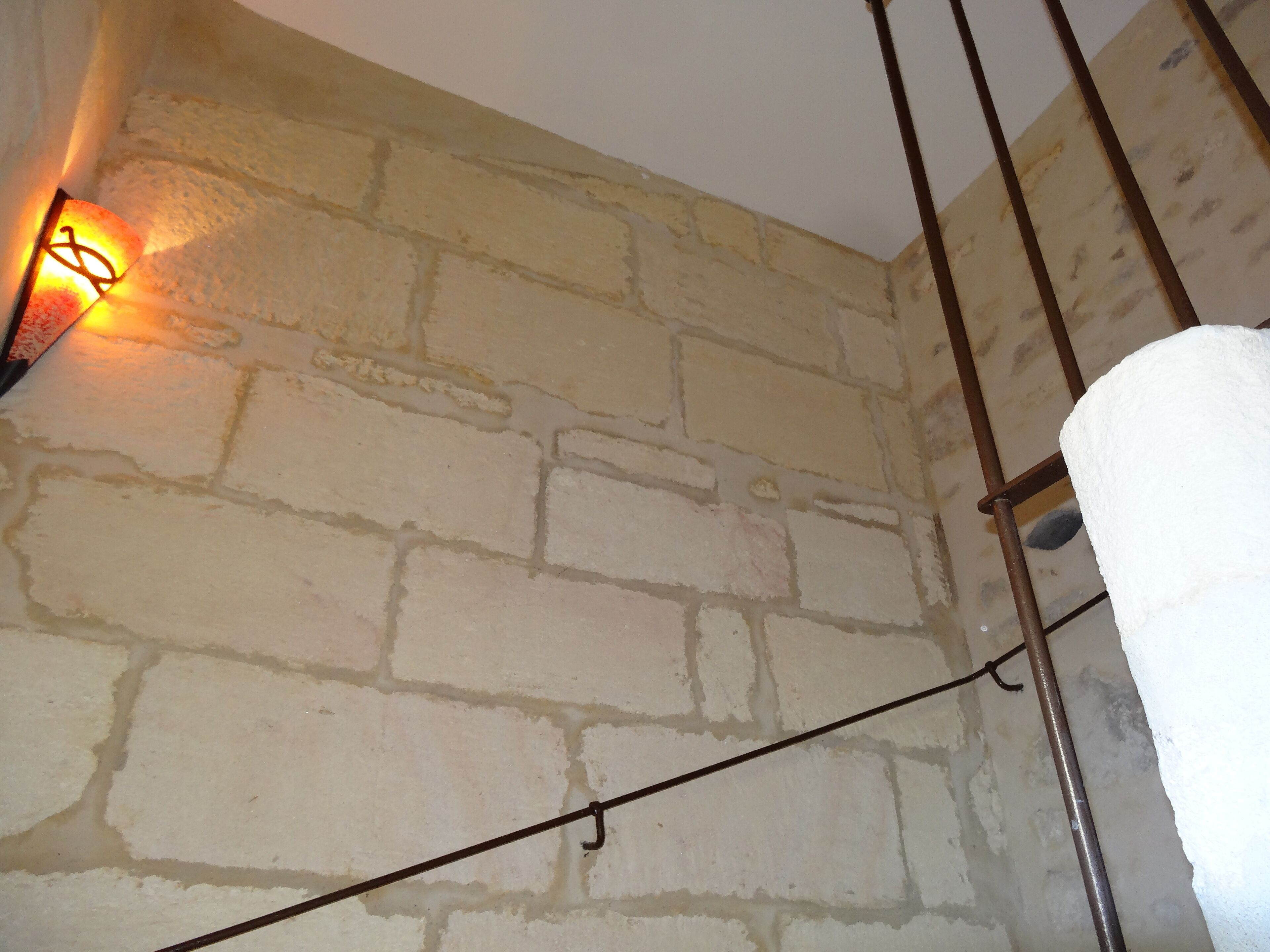 Un mur en pierre avec une rambarde en métal et un luminaire suspendu.