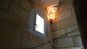 Une pièce aux murs de pierre, dotée d’une petite fenêtre et d’un luminaire fixé au mur.