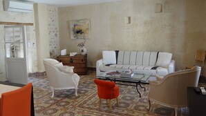 Un salon avec un canapé blanc, deux fauteuils blancs, une table basse en verre et un sol à motifs.