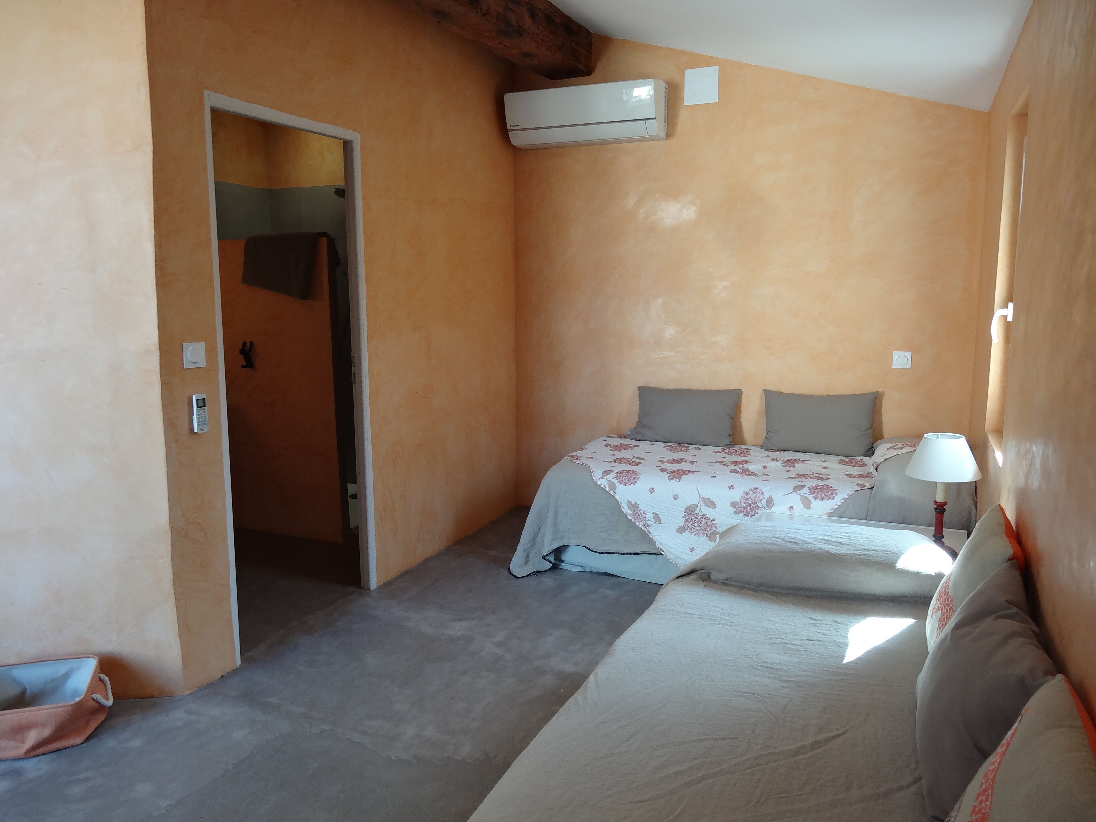 A small, cozy room with a bed, a bedside lamp, and an air conditioning unit on the wall.