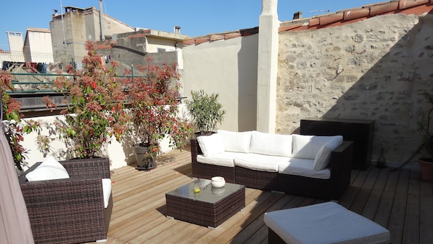 Une terrasse en bois avec un canapé en osier, une petite table et une plante en pot.