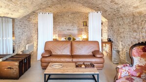 Una habitación acogedora con una pared de piedra, un sofá de cuero, una mesa de centro de madera y un sillón con estampado floral.