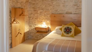 Un dormitorio con techo de piedra, un armario de madera, una mesita de noche con lámpara, una cama con ropa de cama a rayas y un cojín decorativo.