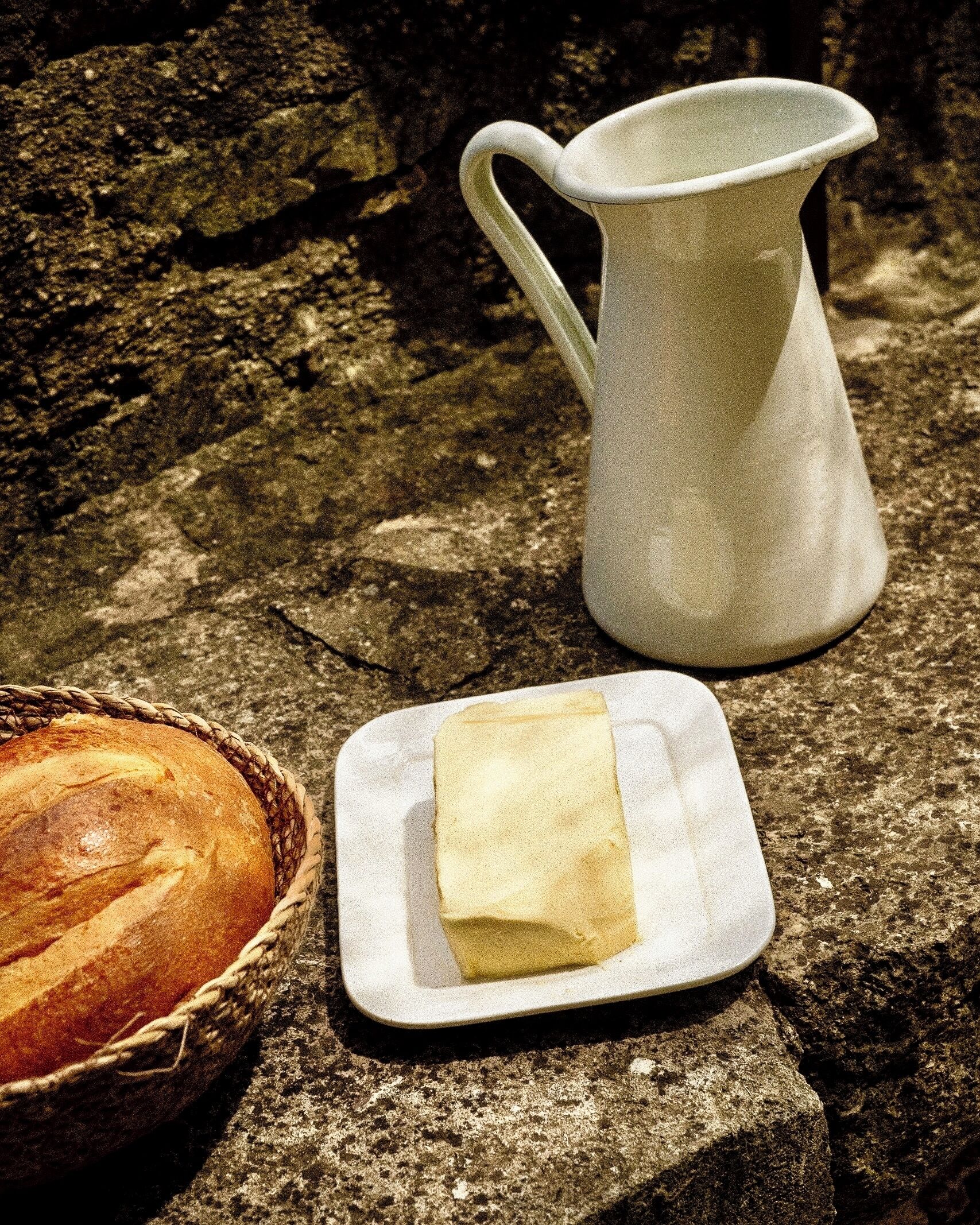 Une miche de pain, un beurrier et une carafe sur une surface en pierre.