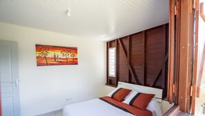 A bedroom with a bed, a painting, a window with wooden shutters, and a door. - Villa F3 standing and all comfort in Petit-Bourg in Guadeloupe (PETIT-BOURG)