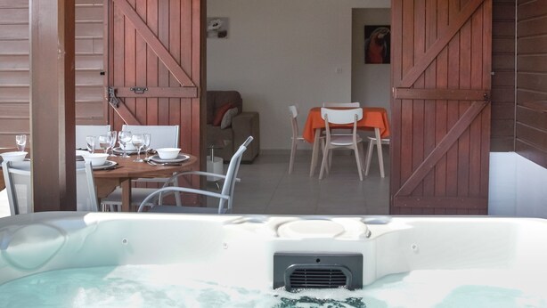 A room with a hot tub, wooden shutters, a dining table with chairs, and a sofa. - Villa F3 standing and all comfort in Petit-Bourg in Guadeloupe (PETIT-BOURG)