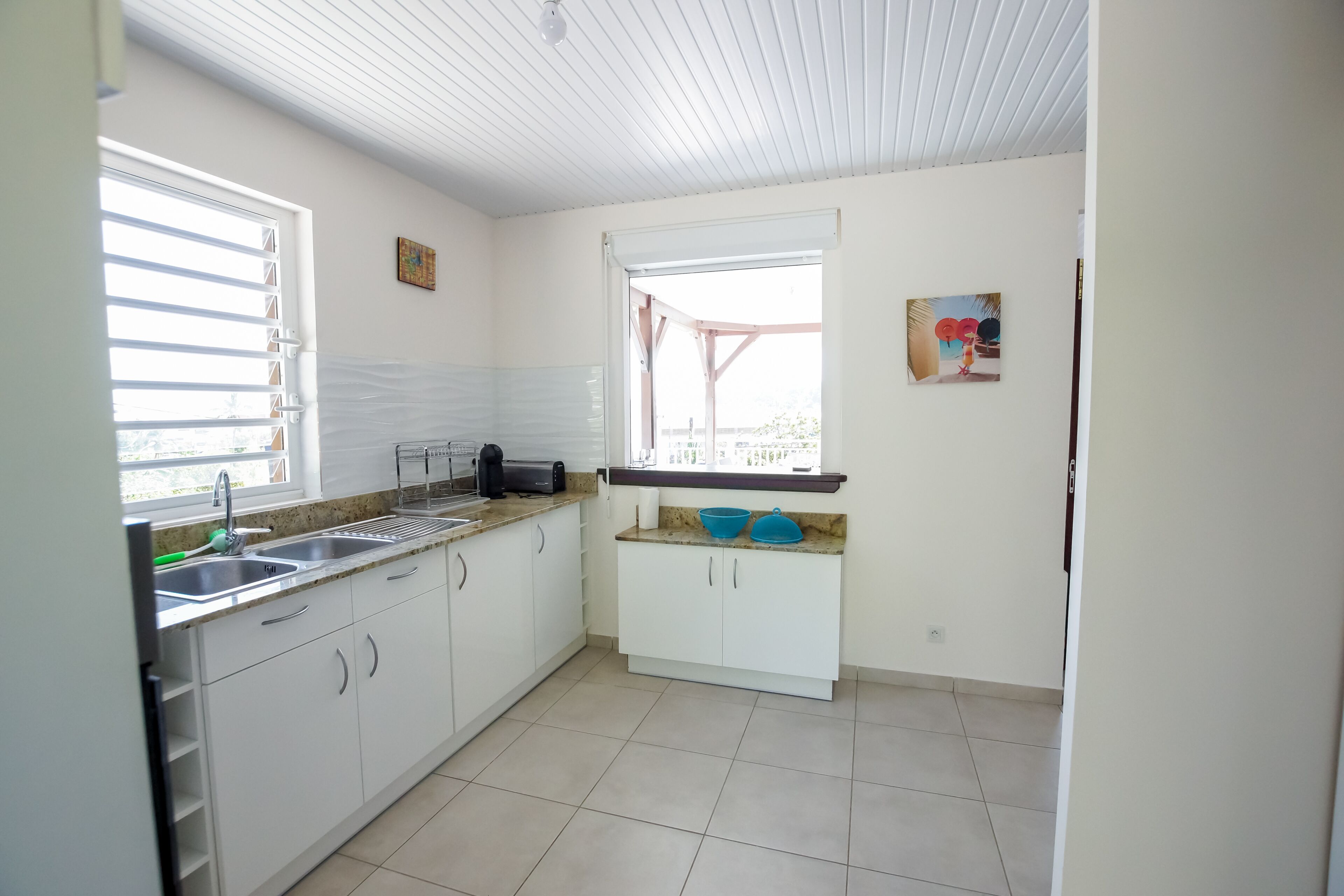 A kitchen with white cabinets, a countertop, a sink, and a window with blinds.
