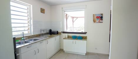 A kitchen with white cabinets, a countertop, a sink, and a window with blinds.