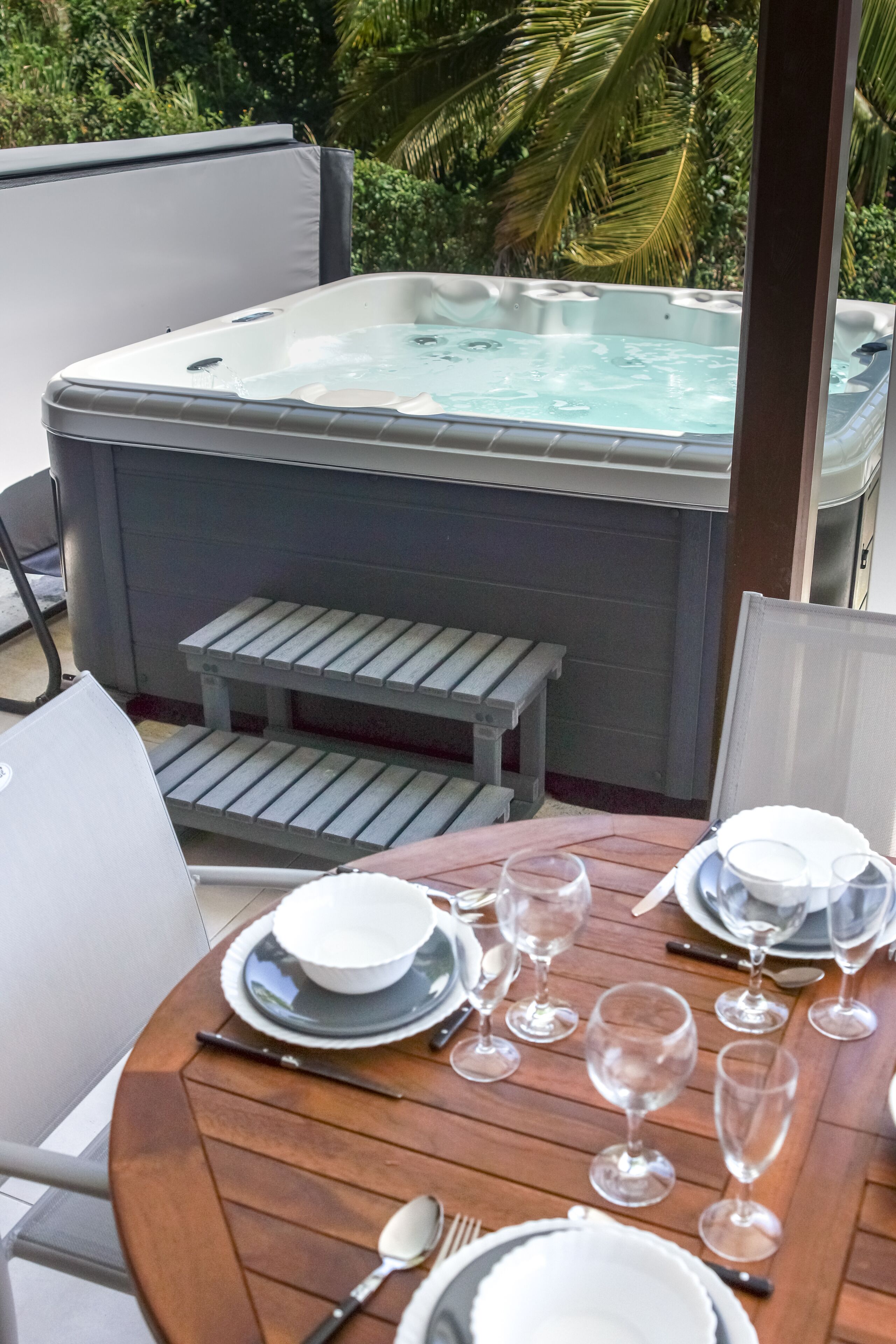 Ein Whirlpool mit Holzterrasse und Essplatz, umgeben von üppiger Vegetation.