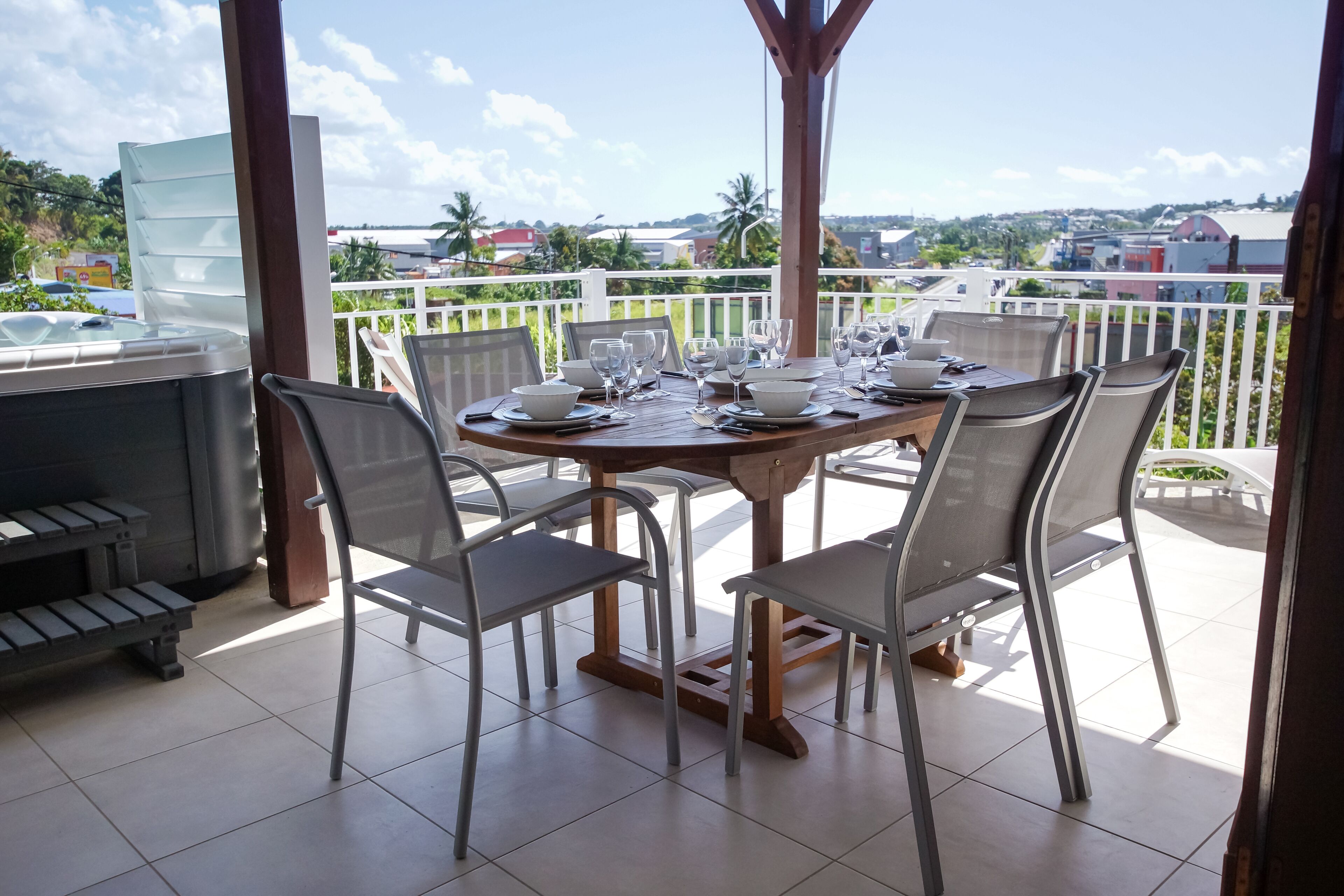 Un área de comedor al aire libre techada con una mesa preparada para cuatro personas, sillas alrededor y una parrilla a la izquierda.