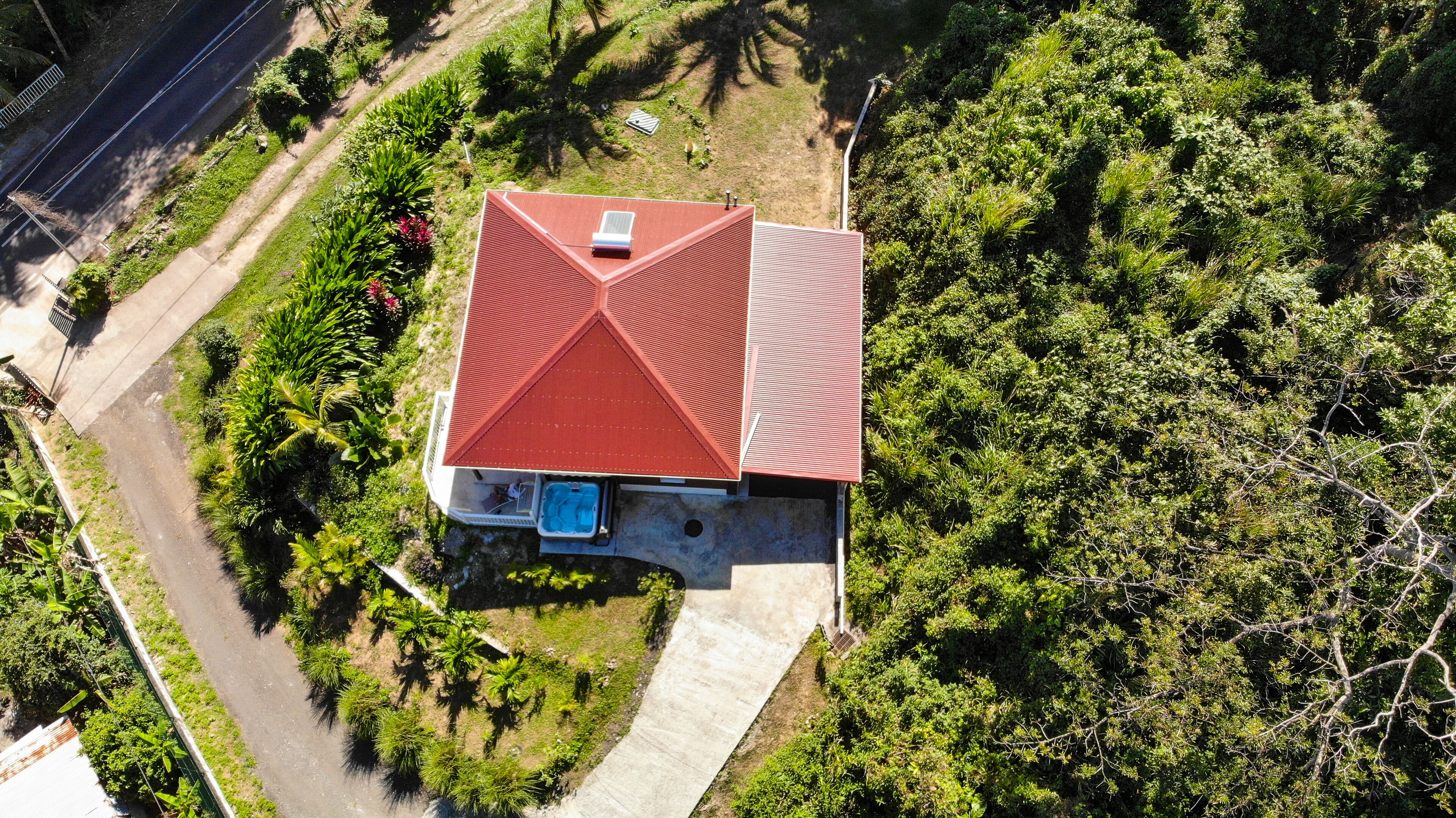 A house with a red roof, surrounded by lush greenery and a paved driveway.