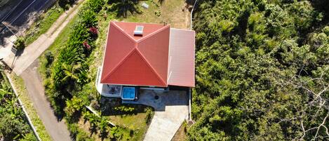 A house with a red roof, surrounded by lush greenery and a paved driveway.