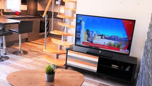 Ett modernt kök med en inbyggd ugn, en matplats med ett träbord och stolar samt en tv som visar en stadsbild.