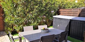 A patio with a table and chairs, surrounded by a wooden fence and lush greenery.