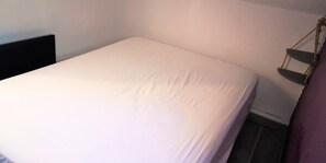 A small, single-bed room with a white bedspread, a black headboard, and a simple, uncluttered layout.