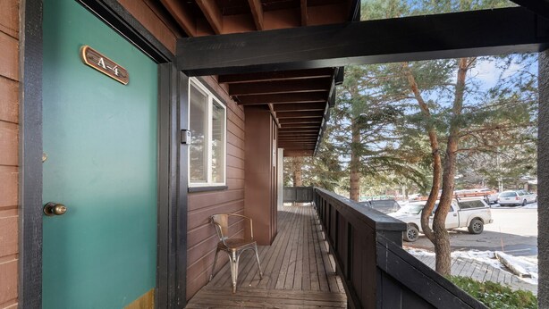 A wooden porch with a green door labeled "A-4", a metal chair, and a view of a parking lot with cars and trees. - RMR: Gros Ventre A4 Condo in Teton Village (Teton Village)