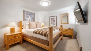 A bedroom with a wooden bed, two bedside tables, a nightstand, a TV mounted on the wall, and two framed pictures on the wall. - RMR: Gros Ventre A4 Condo in Teton Village (Teton Village)