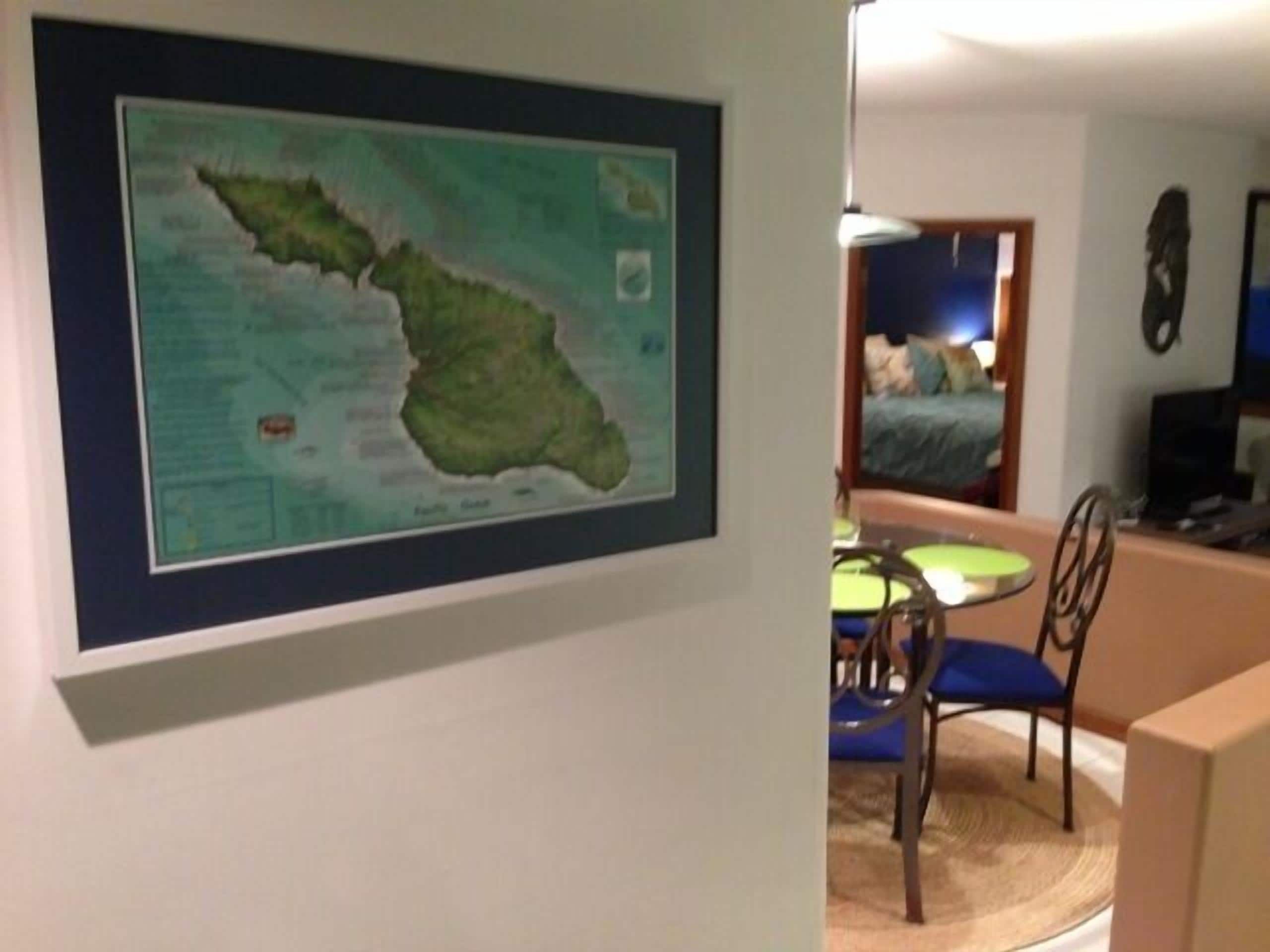 A framed map on a wall, a dining area with a table and chairs, and a bed in the background.
