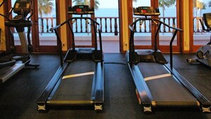 Een sportschool met loopbanden en fitnessapparatuur, grote ramen met uitzicht op de oceaan.