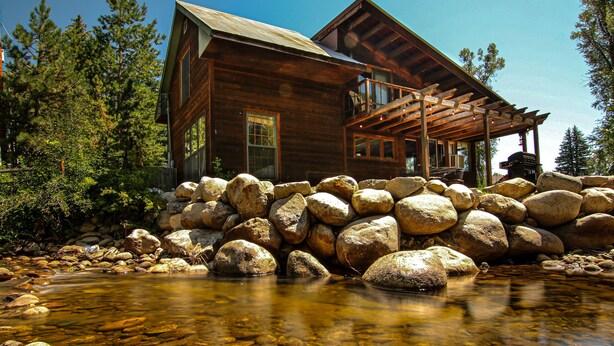 A wooden cabin with a stone foundation, a clear stream in front, and a wooden deck. - Private Cabin in beautiful Downtown Steamboat! BEST LOCATION in OLD TOWN! (Steamboat Springs)