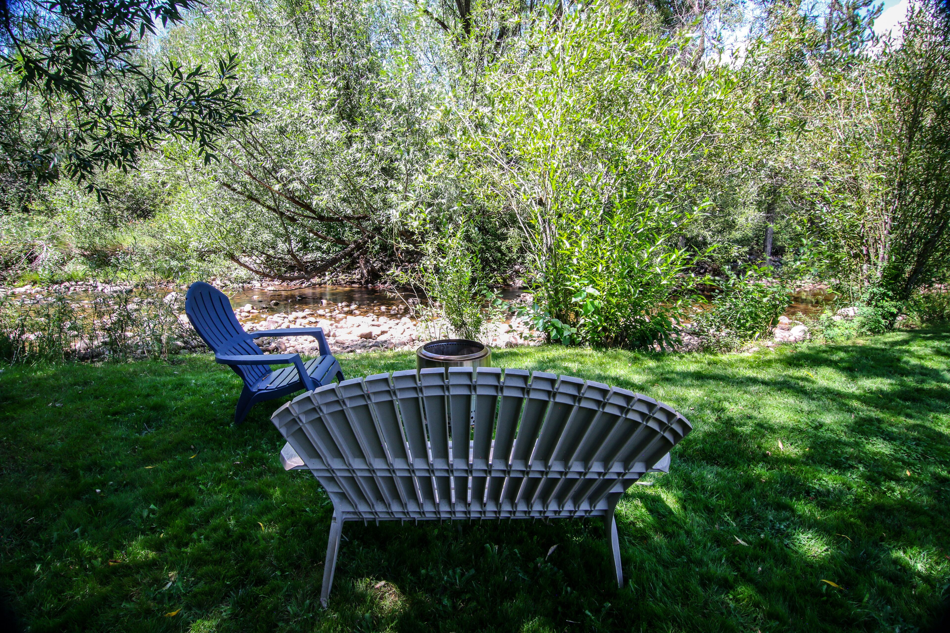 Un jardín con una silla de metal y una mesa, rodeado de follaje y árboles.