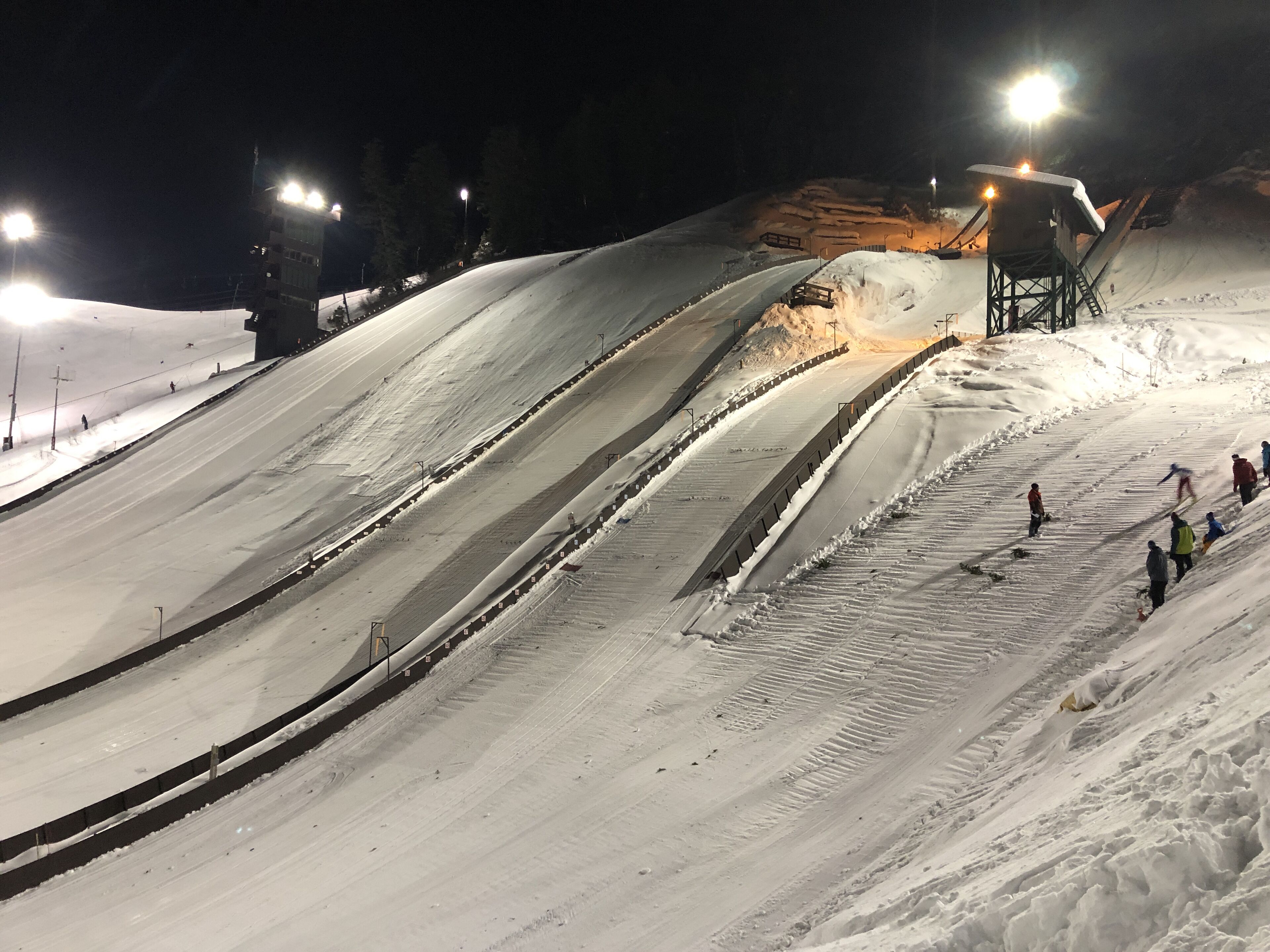 Une piste de ski enneigée, illuminée par des projecteurs, de nuit.