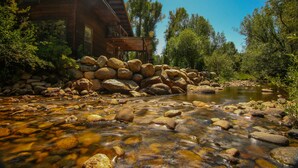A wooden cabin with a stone foundation, surrounded by a natural landscape with a clear stream. - Private Cabin in beautiful Downtown Steamboat! BEST LOCATION in OLD TOWN! (Steamboat Springs)