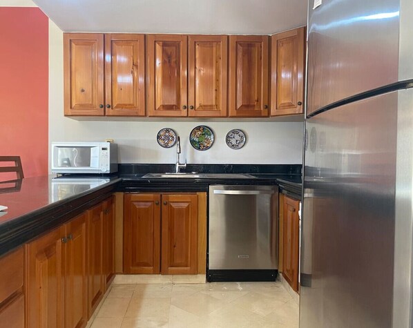A kitchen with wooden cabinets, a stainless steel refrigerator, a microwave, and a dishwasher.