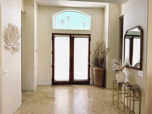 A hallway with a double door, a large window with a view of palm trees, and a mirror on the wall.