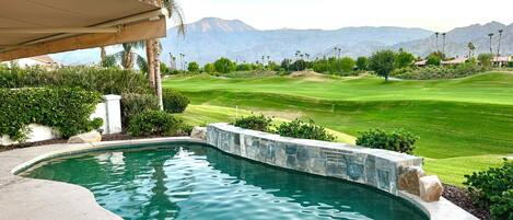 A swimming pool with a view of a golf course and mountains in the background.