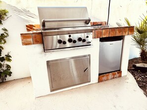Een buitenbarbecue met een roestvrijstalen afwerking, een bedieningspaneel met knoppen en een kleine koelkast.