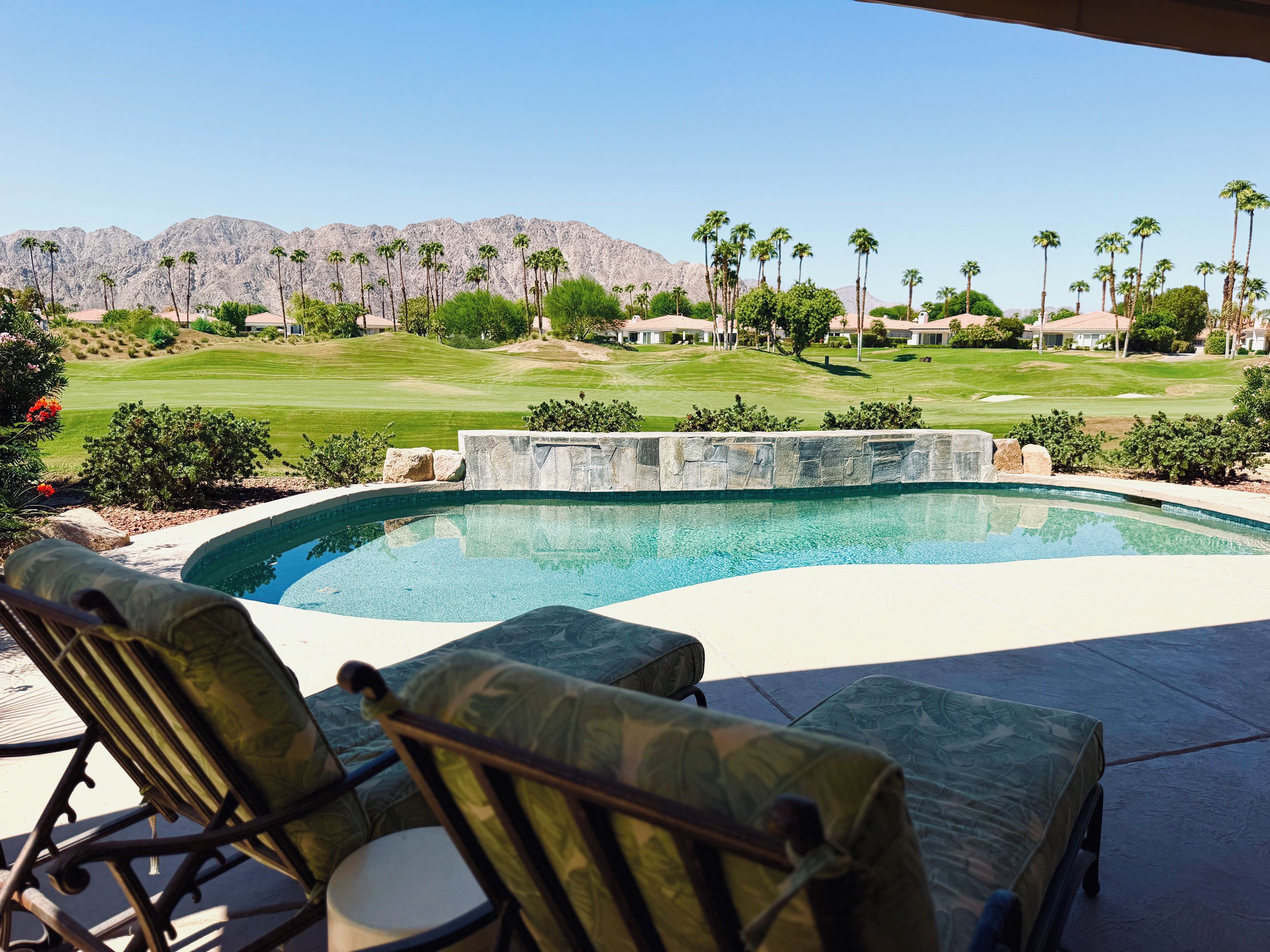 A swimming pool with a view of a golf course and mountains in the background.