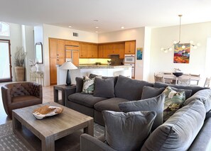 A modern living room with a sofa, coffee table, and a dining area with a table and chairs.