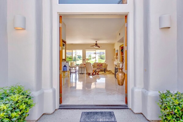 A modern entrance with a clear view into a well-lit living area featuring a sofa, chairs, and a coffee table. - Breathtaking views from your private pool & spa in PGA West: 3 BD/STR #065869 (La Quinta)