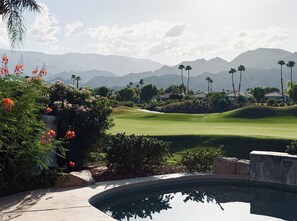 Un parcours de golf avec une piscine, des palmiers et des montagnes en arrière-plan.