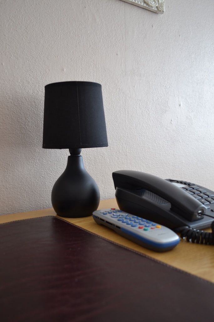 Un escritorio con una lámpara, un teléfono y un control remoto.