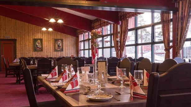 A restaurant with wooden walls and large windows, tables set with flags, and a red carpet. - Bardu Hotell (Bardu)