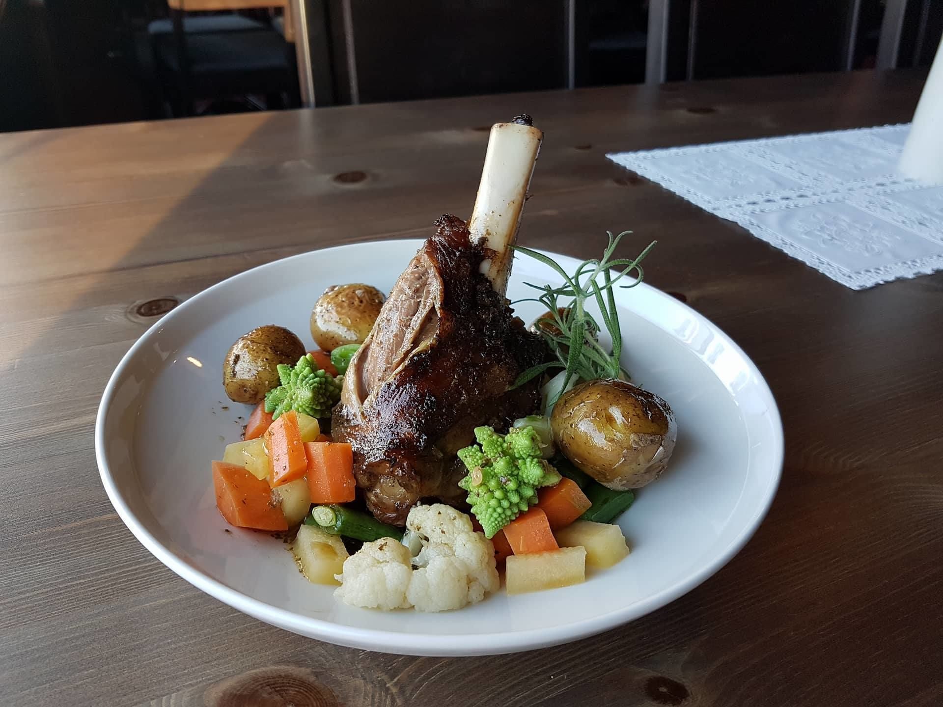 A plate of food with a roasted meat, potatoes, and vegetables on a wooden table.