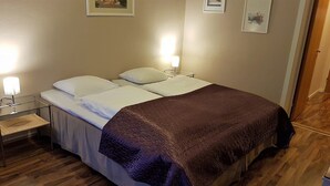 A neatly made bed with white linens and a brown blanket, a bedside table with a lamp, and a wooden floor. - Bardu Hotell (Bardu)
